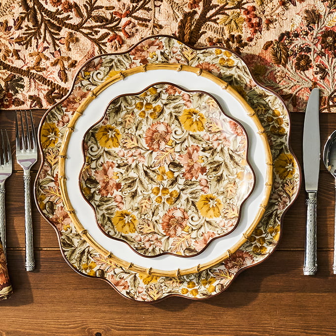 Decorative floral plate on a wooden table with cutlery and a patterned tablecloth.