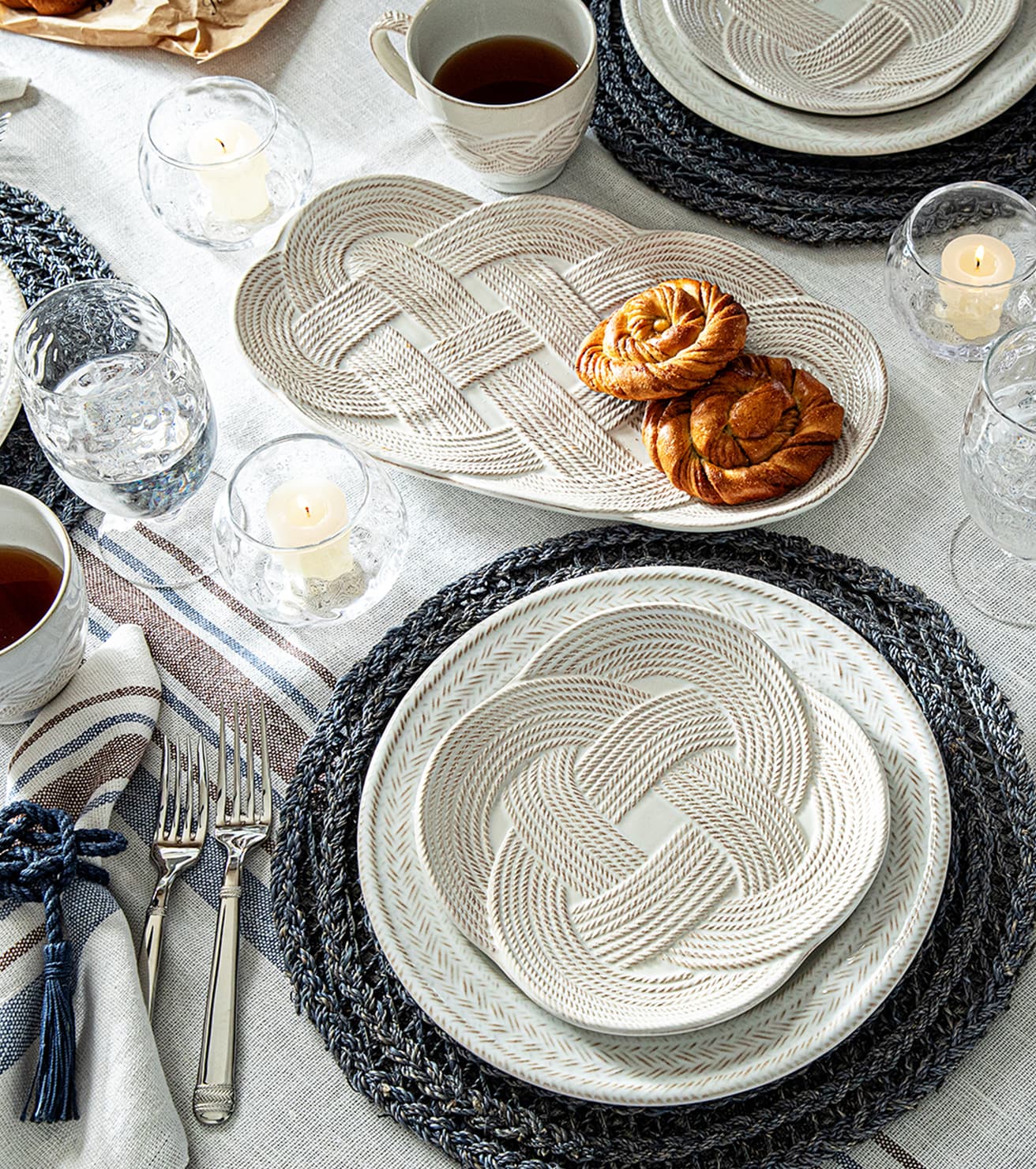 Dining table setting with woven placemats and plates, candles, and tea.
