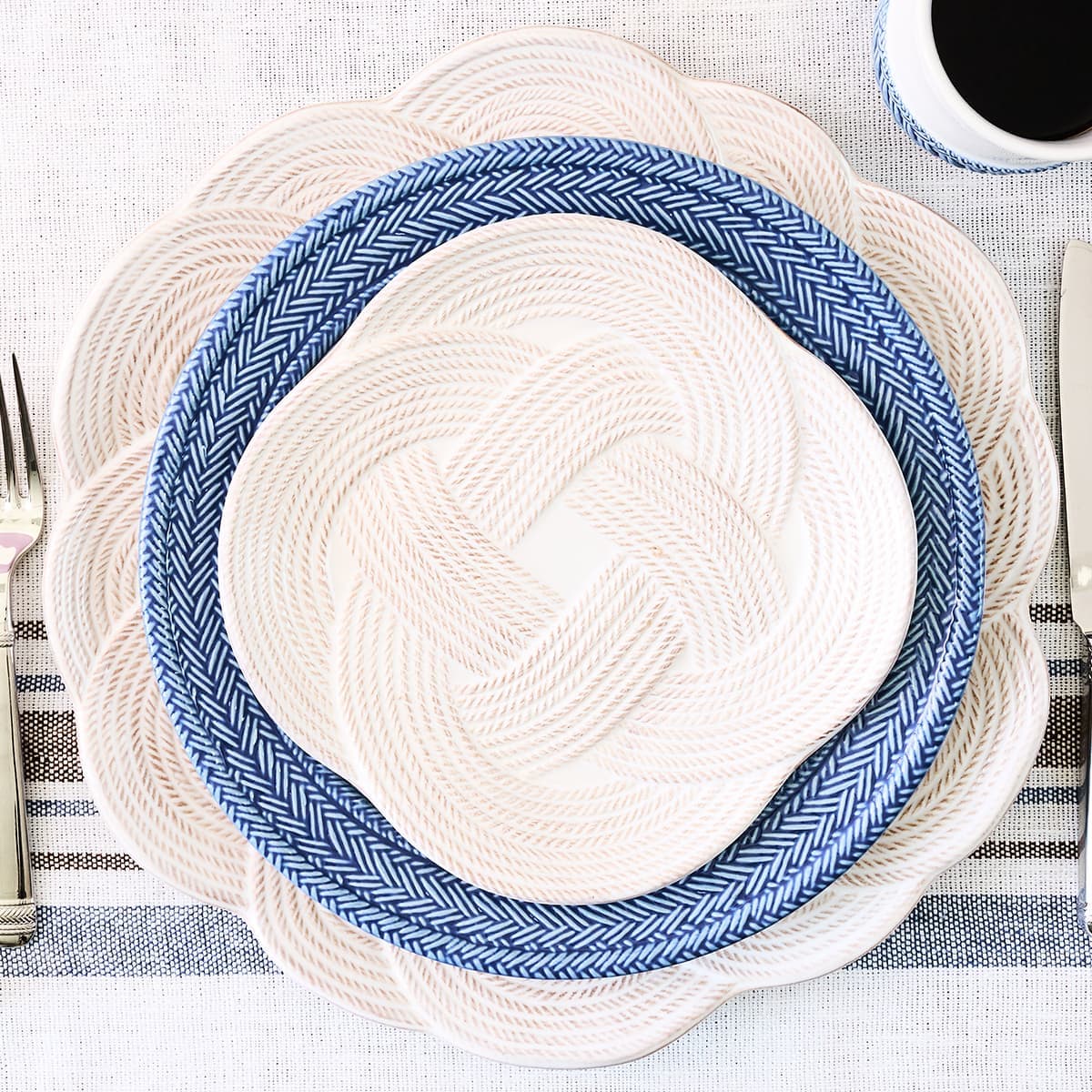 Set of woven placemats with blue and white patterns on a striped tablecloth.