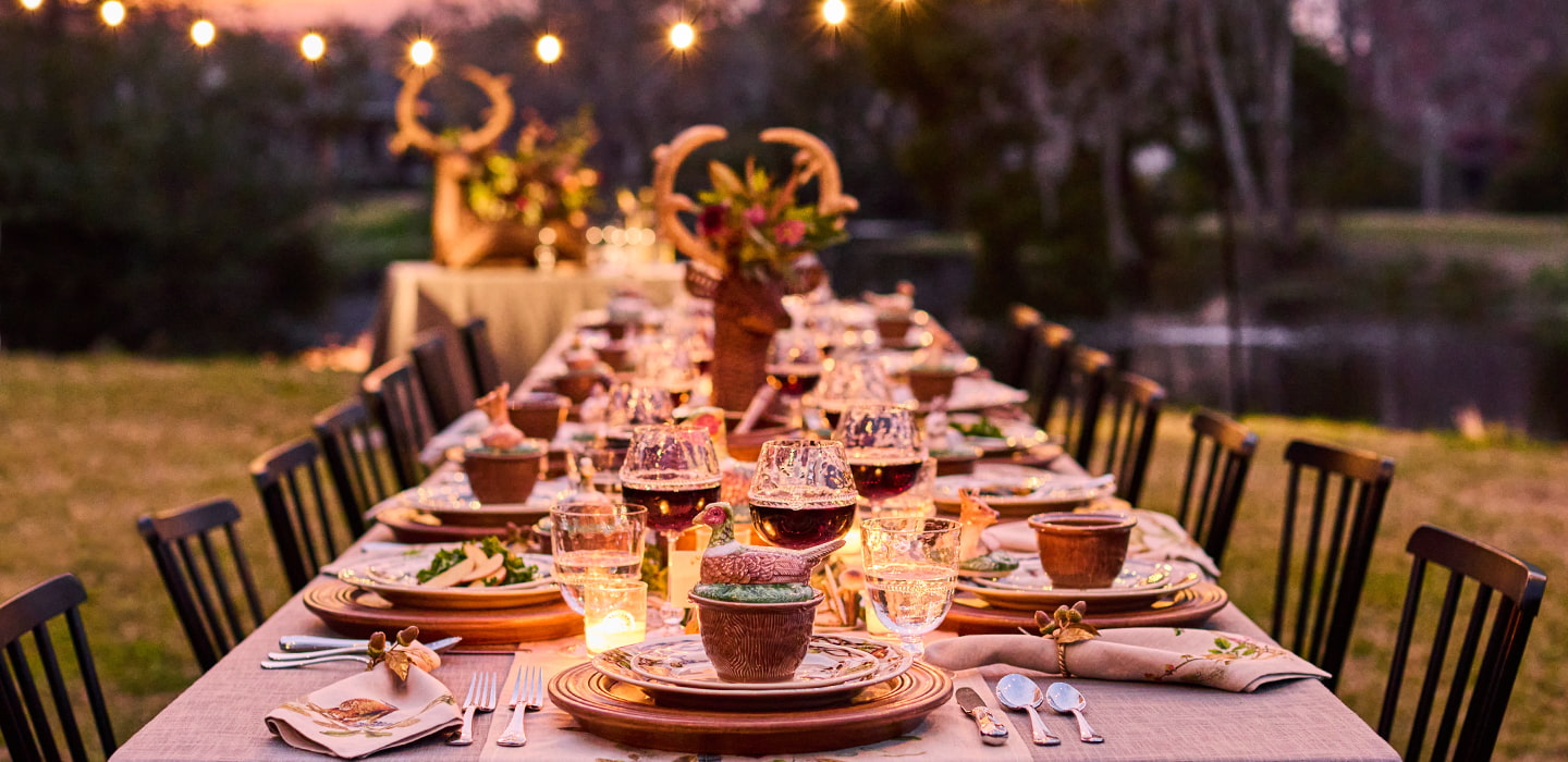 Dining table set for an outdoor dinner party with candles and glasses in a garden setting.