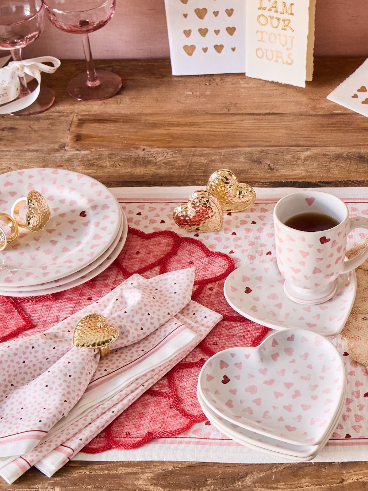 Valentine's Day table setting with heart-themed plates, napkins, and a cup of coffee on a wooden table.