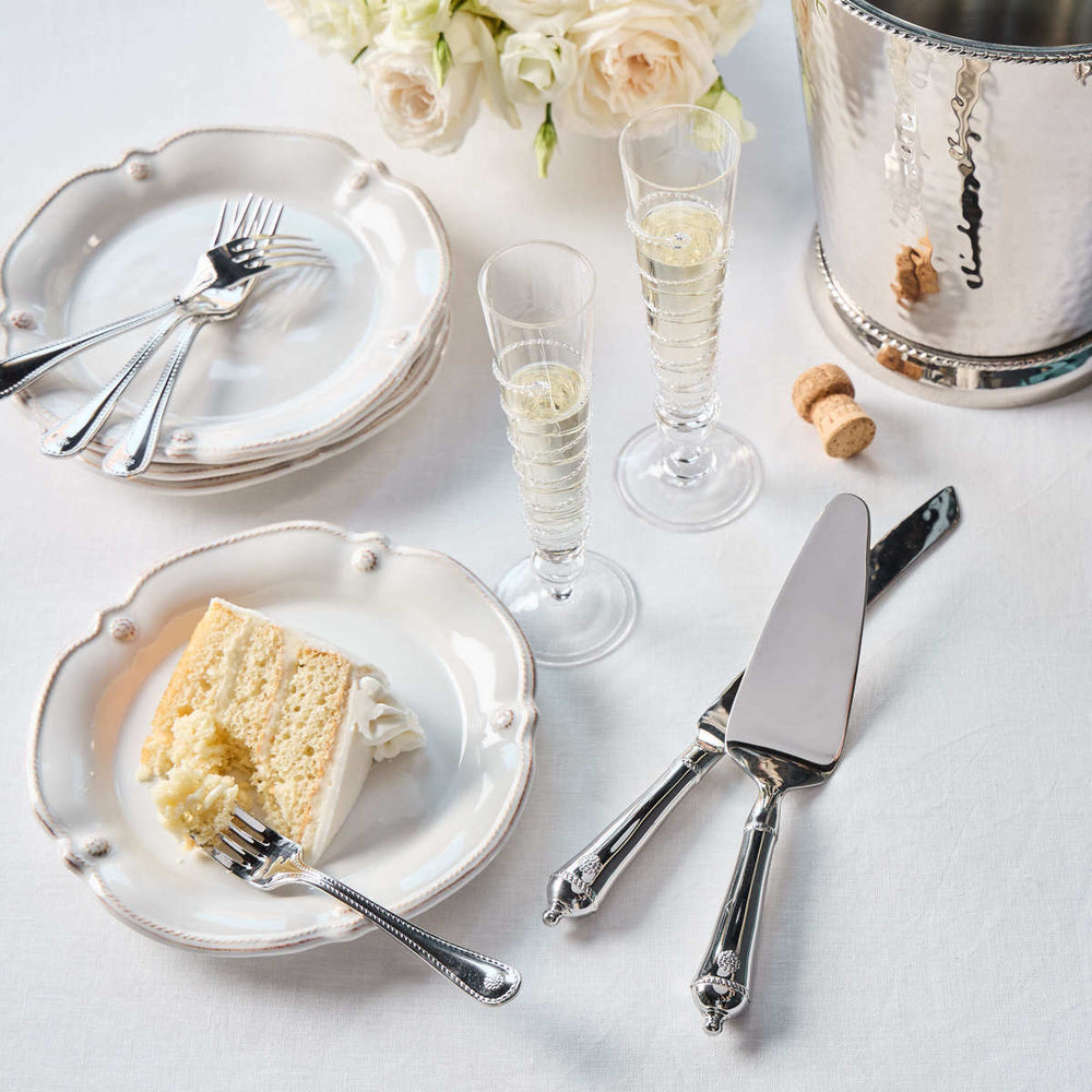 Table setting with cake, champagne flutes, and silverware on a light surface.
