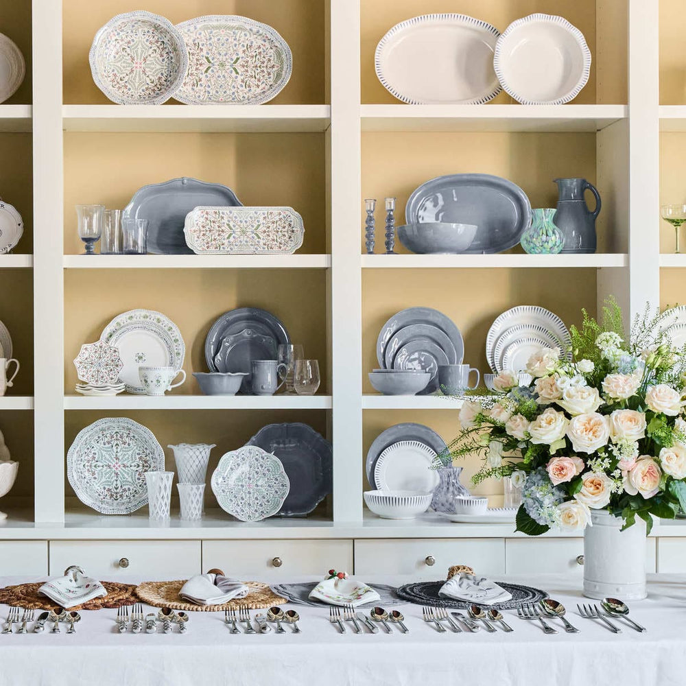 Registry room with shelves displaying various ceramic plates and bowls, a table set with cutlery and a floral arrangement.