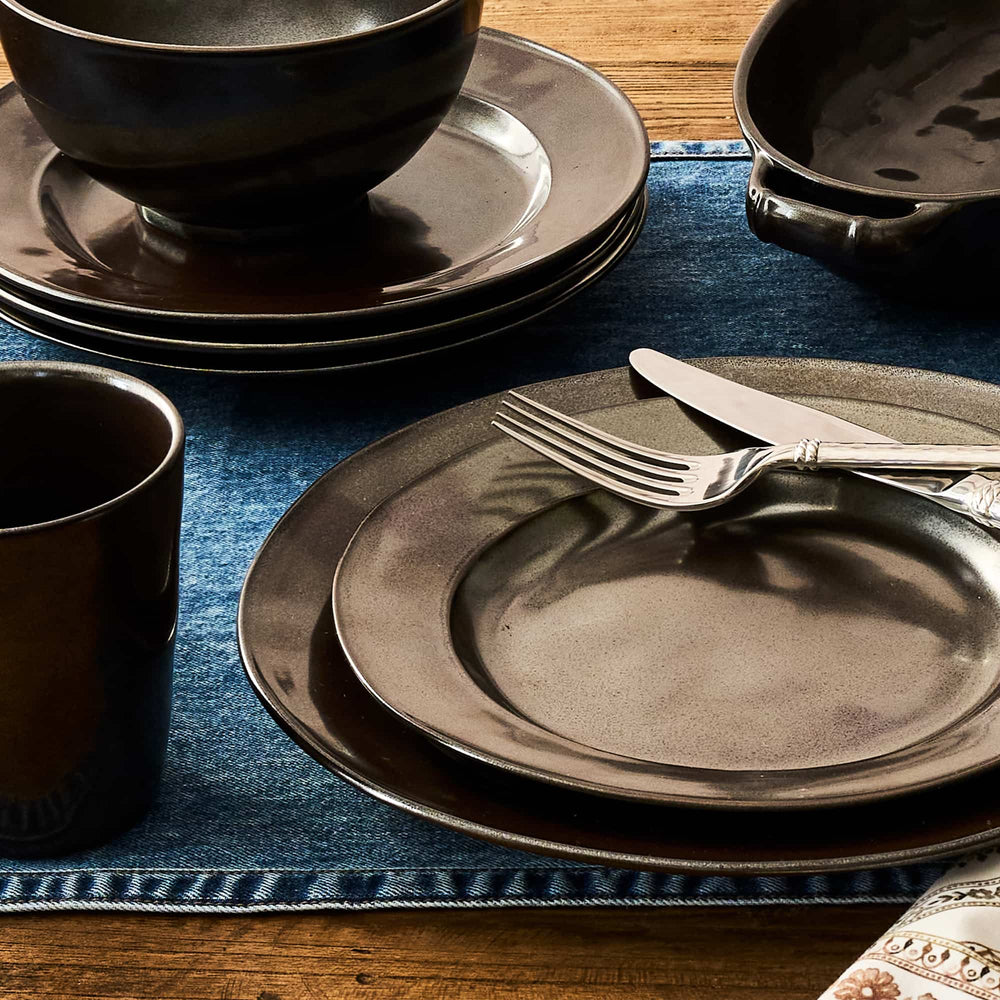 Set of dark ceramic plates, bowls, and cutlery on a blue placemat.