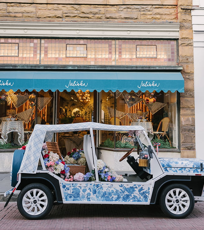 Decorative golf cart with floral patterns in front of a store with a blue awning.