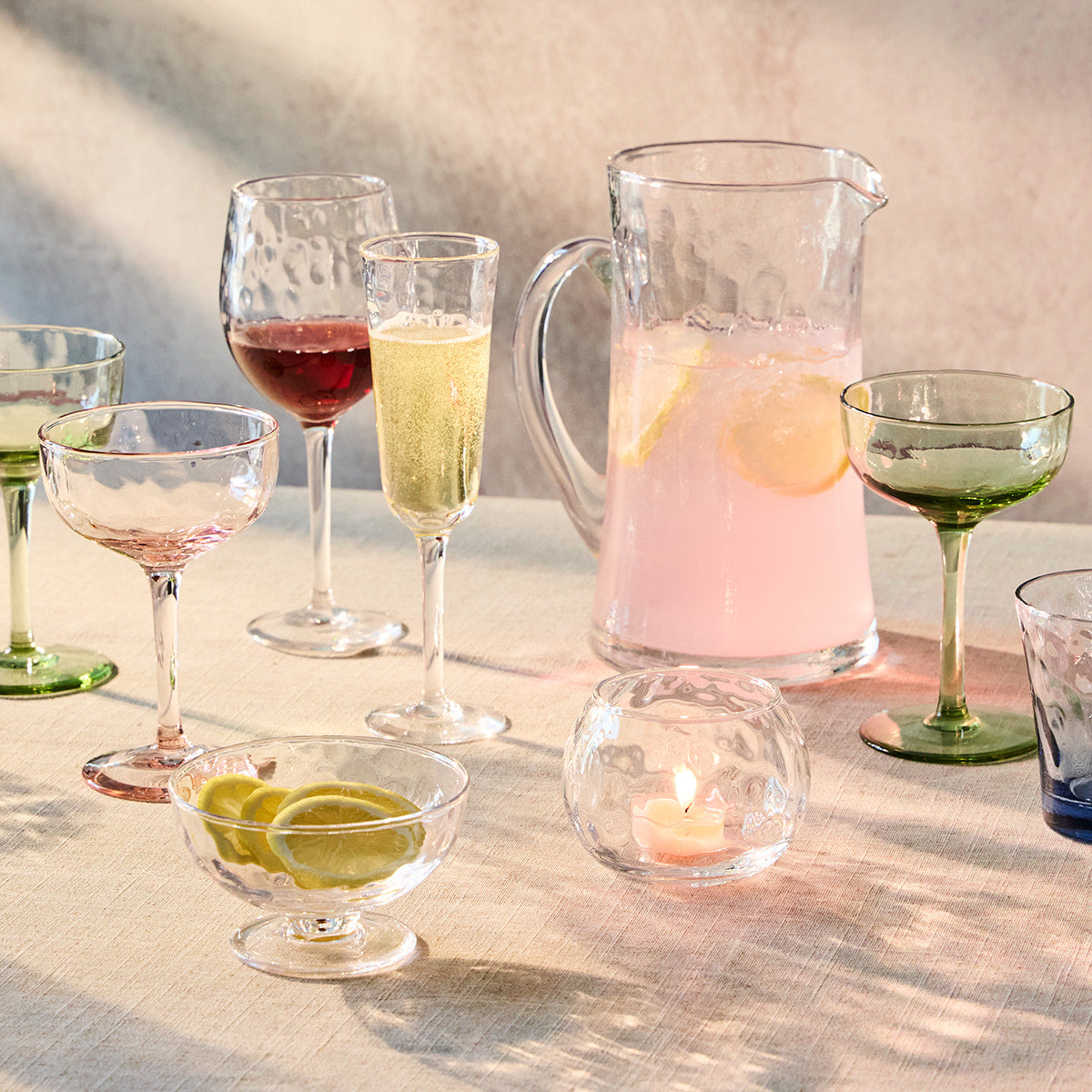 Glassware including a pitcher, wine glasses, and cocktail glasses on a linen tablecloth. 