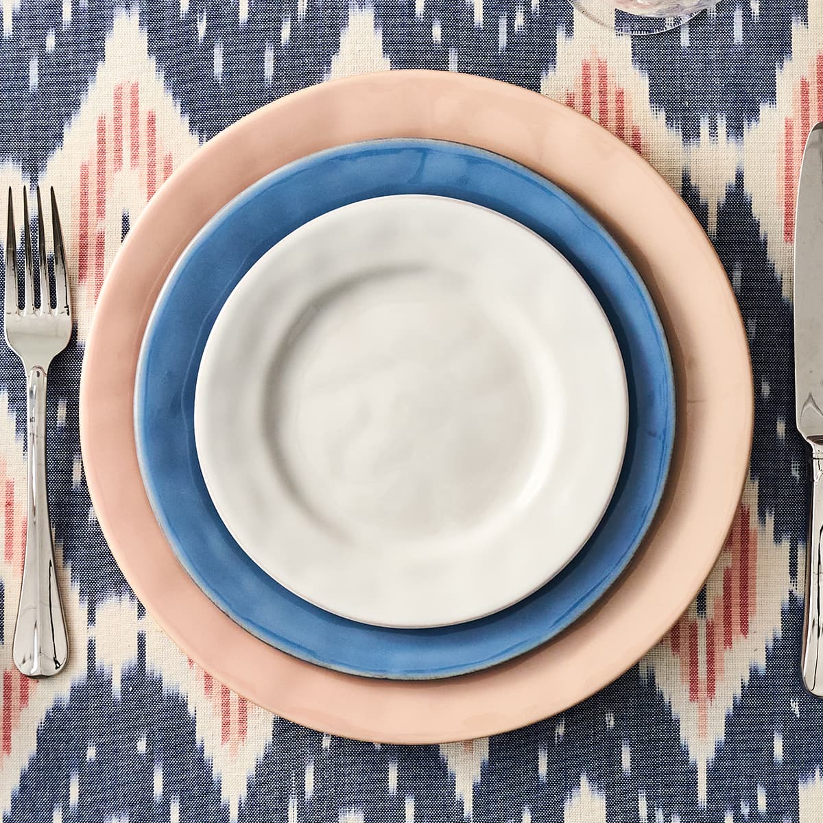 Stack of colorful ceramic plates on a patterned tablecloth with cutlery.