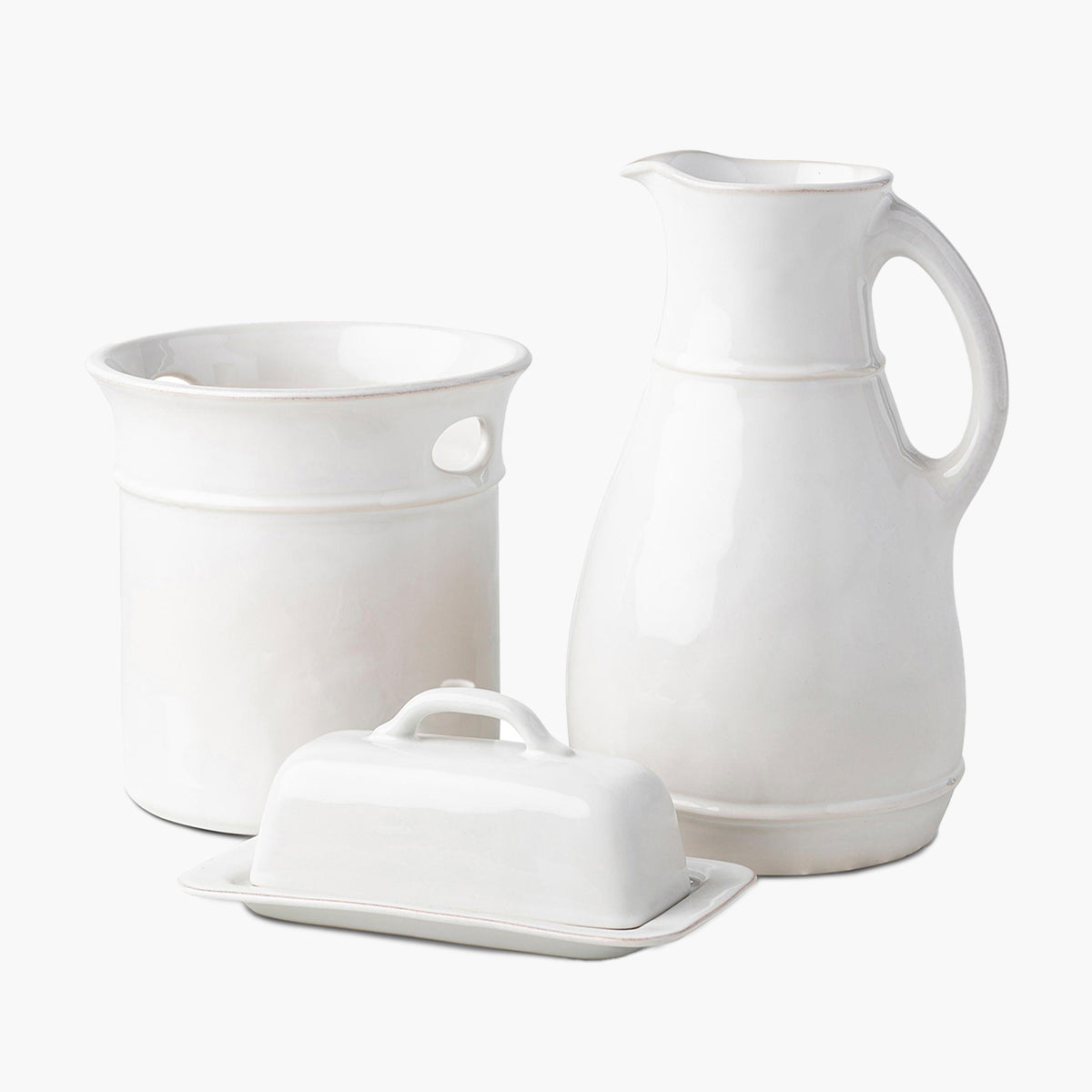 Set of white ceramic kitchen items including a pitcher, a butter dish, and a storage jar on a white background.