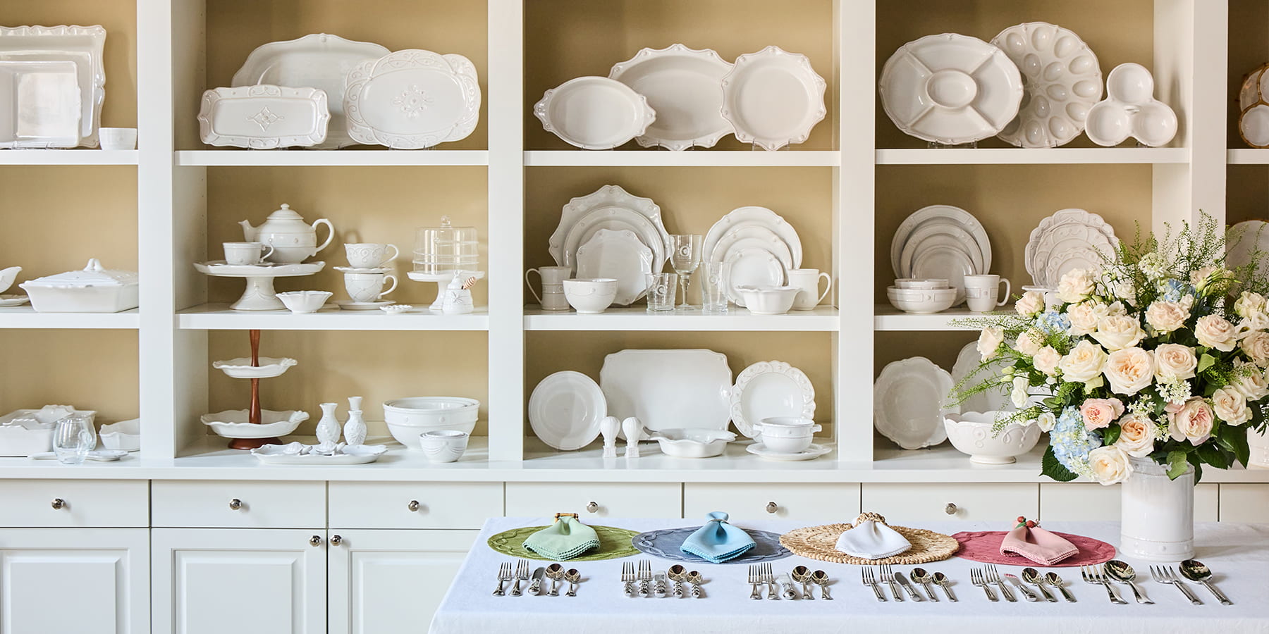 White ceramic dishes and tableware displayed on a white cabinet with a floral arrangement.