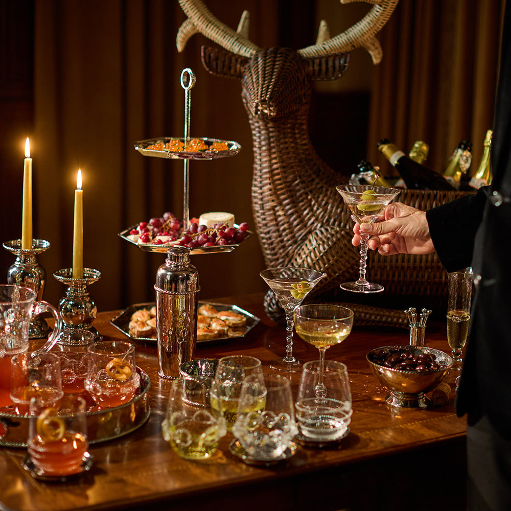 Dinner table with drinks and appetizers, featuring a deer head rattan ice bucket in the background.