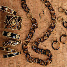 Tortoise, black and gold jewelry is laid out over a cork table top.