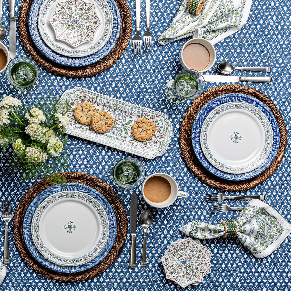 Elegant table setting with blue and white plates, silverware, and a floral centerpiece on a blue patterned tablecloth.