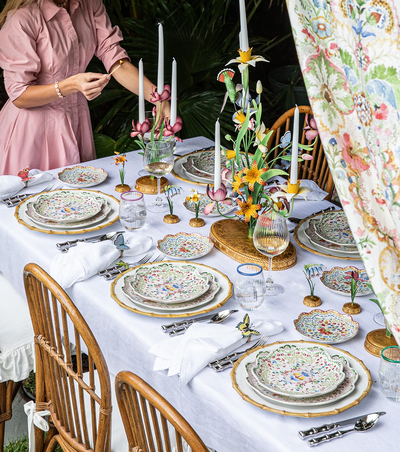 Dining table set with floral centerpieces, candles, and patterned plates in an outdoor setting.