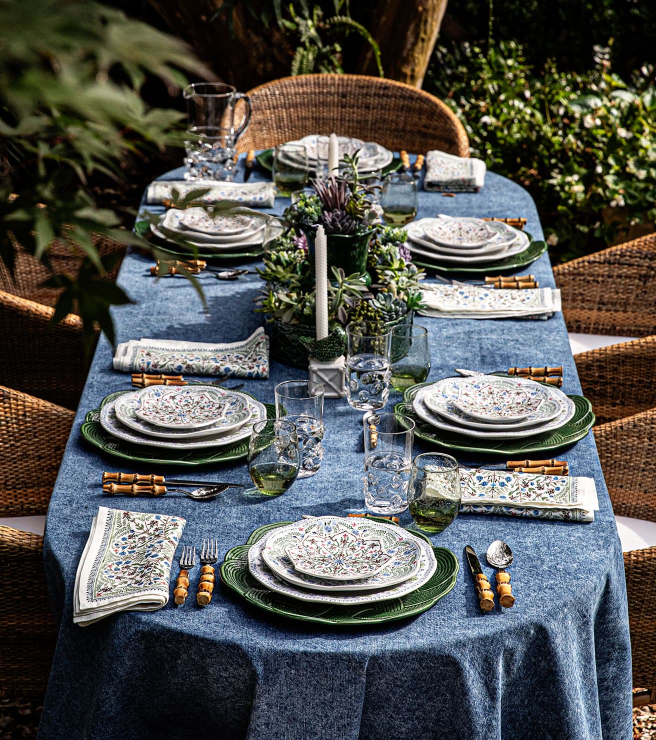 Elegant table setting with blue tablecloth, green plates, and decorative elements in an outdoor setting.