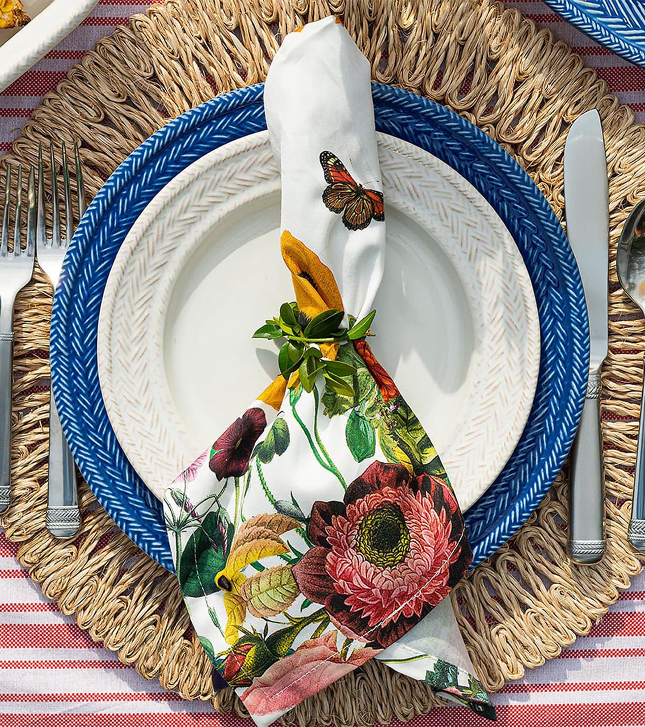 Decorative table setting with floral napkin, blue plate, and wicker placemat. 