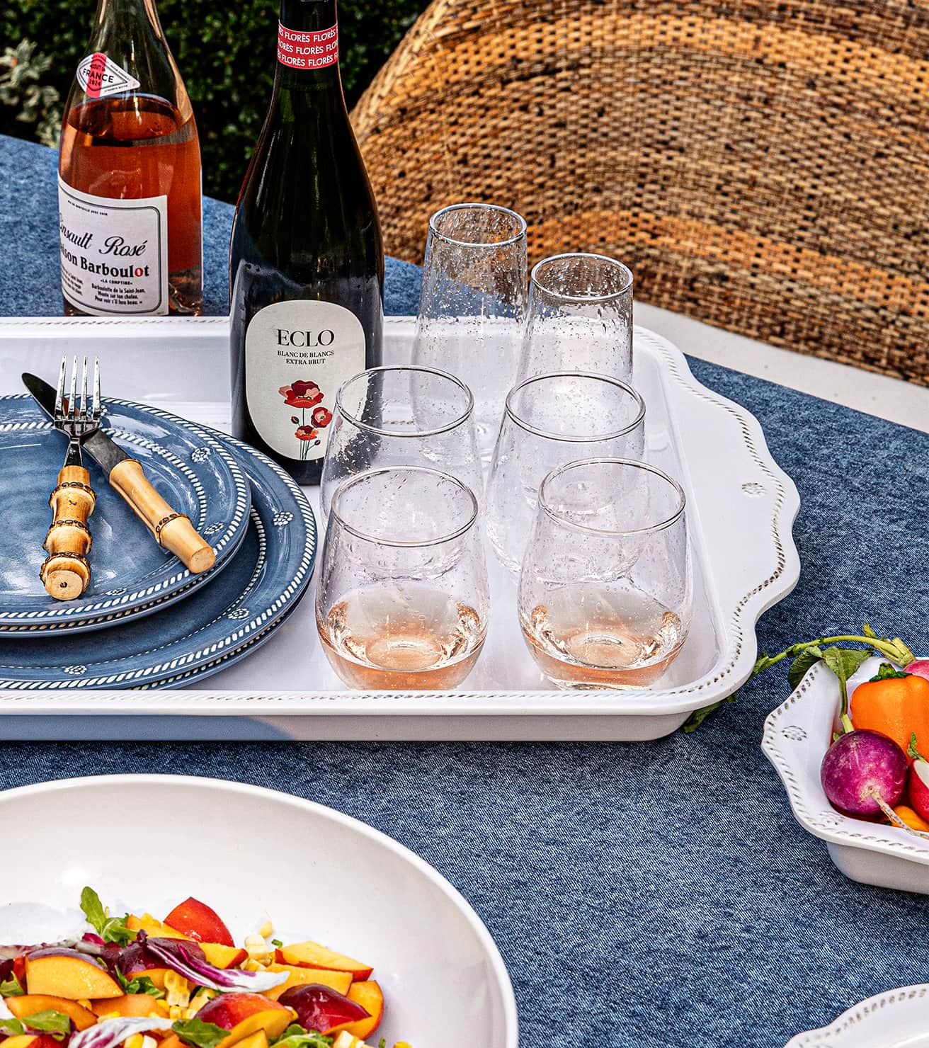 Table setting with wine glasses, bottles, and a salad on a blue tablecloth.