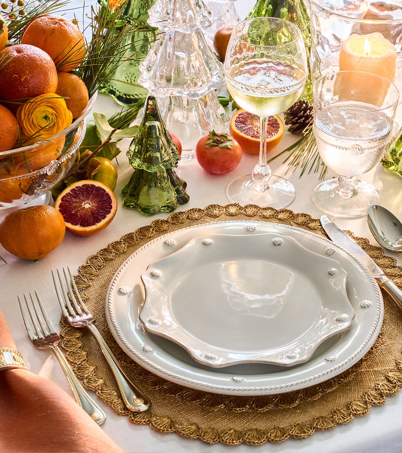 Elegant table setting with white plates, gold chargers, and decorative fruits on a white tablecloth.