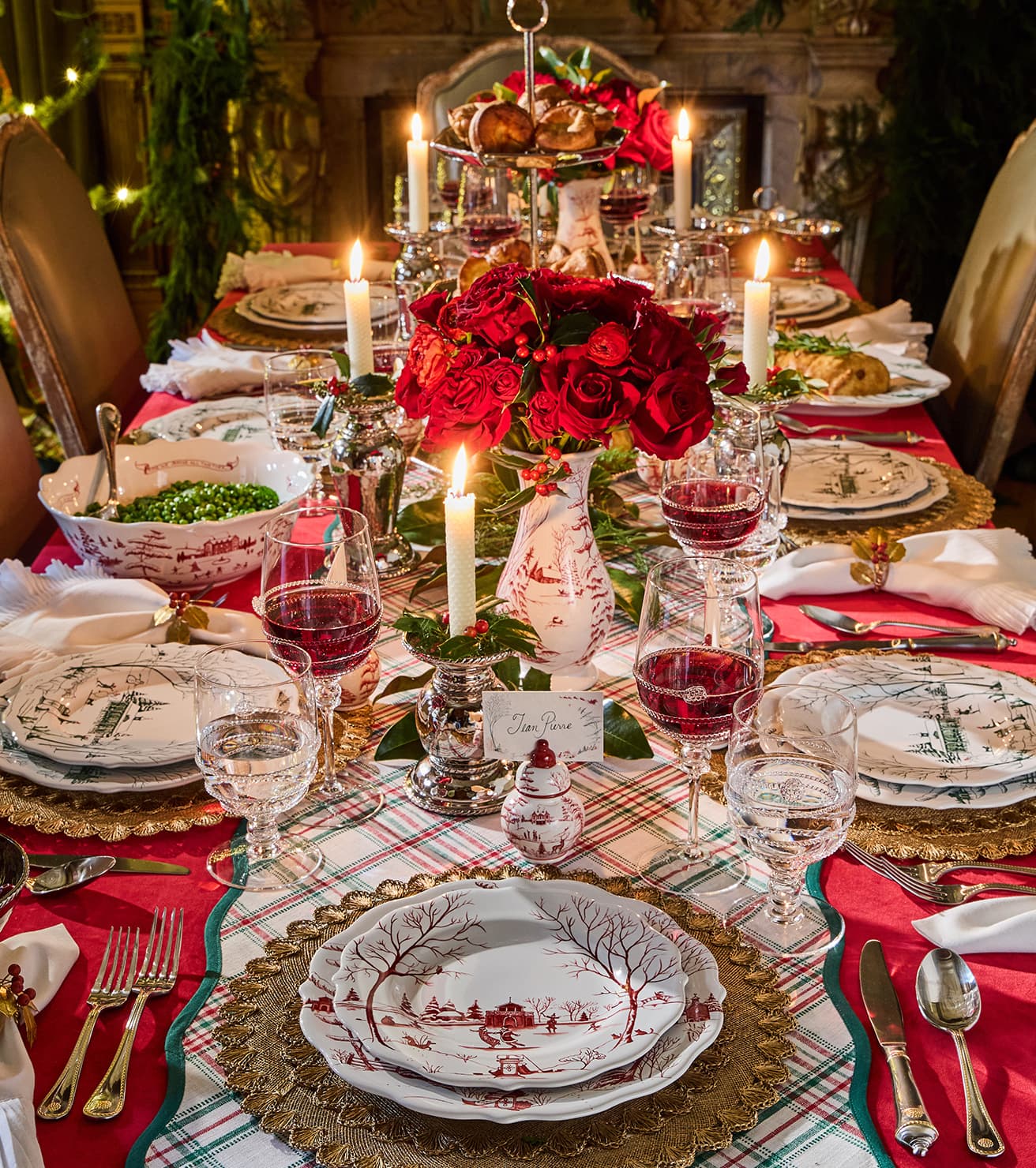 Decorative Christmas table setting with red and gold accents, candles, and floral arrangements.