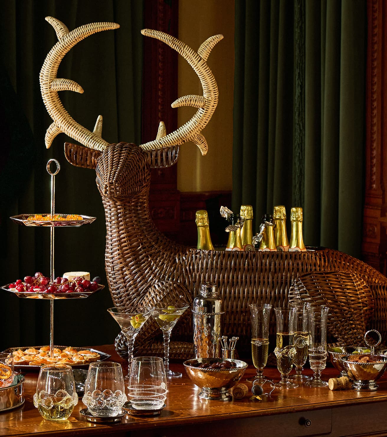 Decorative wicker deer head with bottles and glasses on a table against a dark curtain background