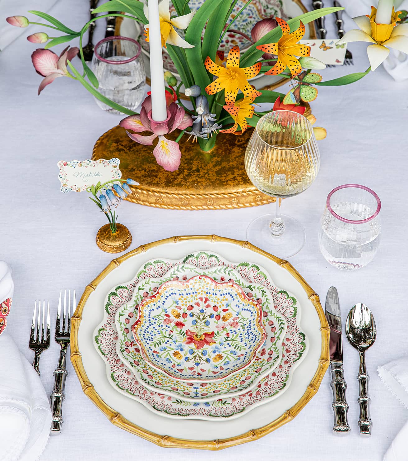 Elegant table setting with floral centerpiece, colorful plates, and silverware on a white tablecloth.