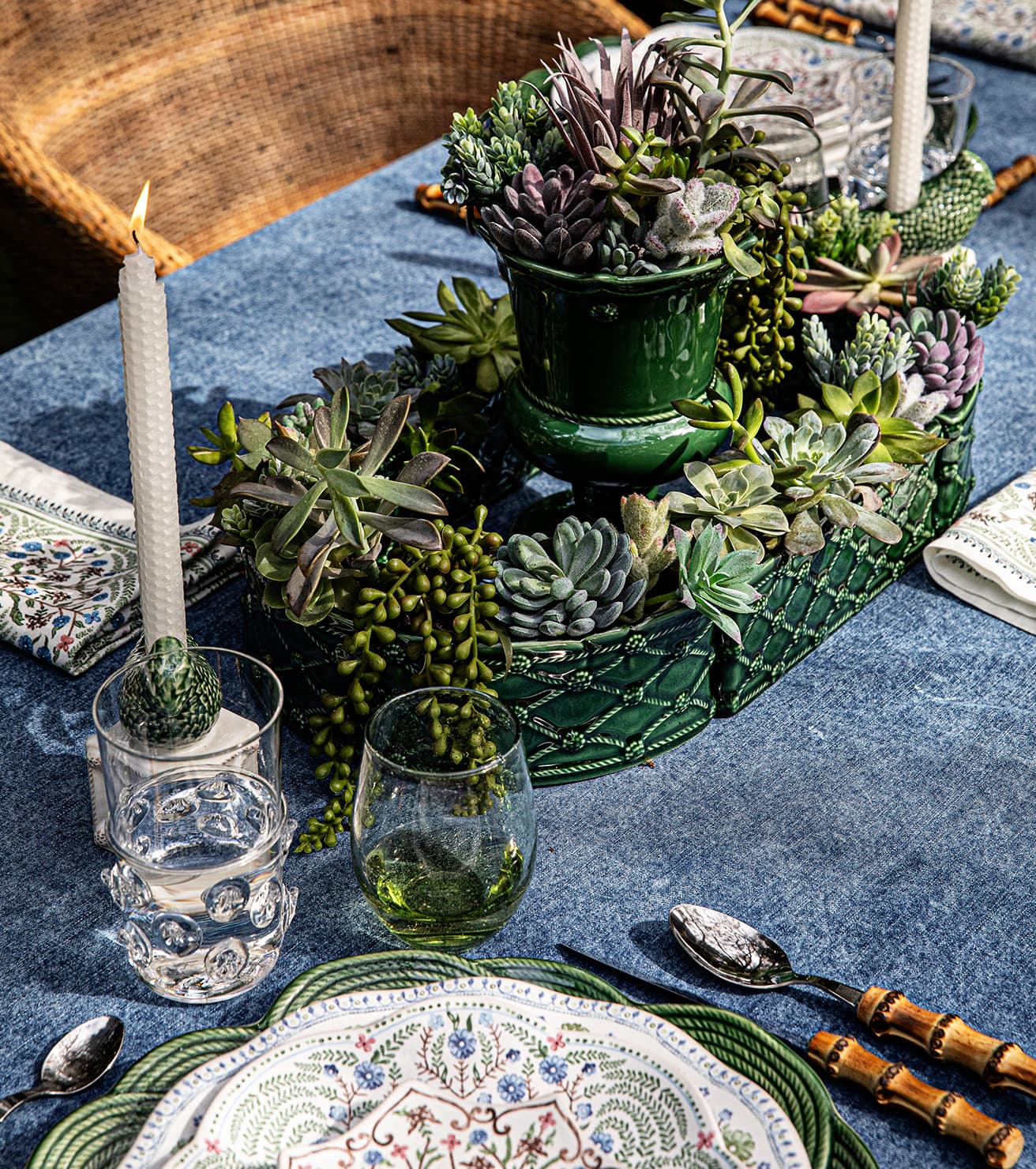 Decorative table setting with succulents, candles, and glassware on a blue tablecloth.