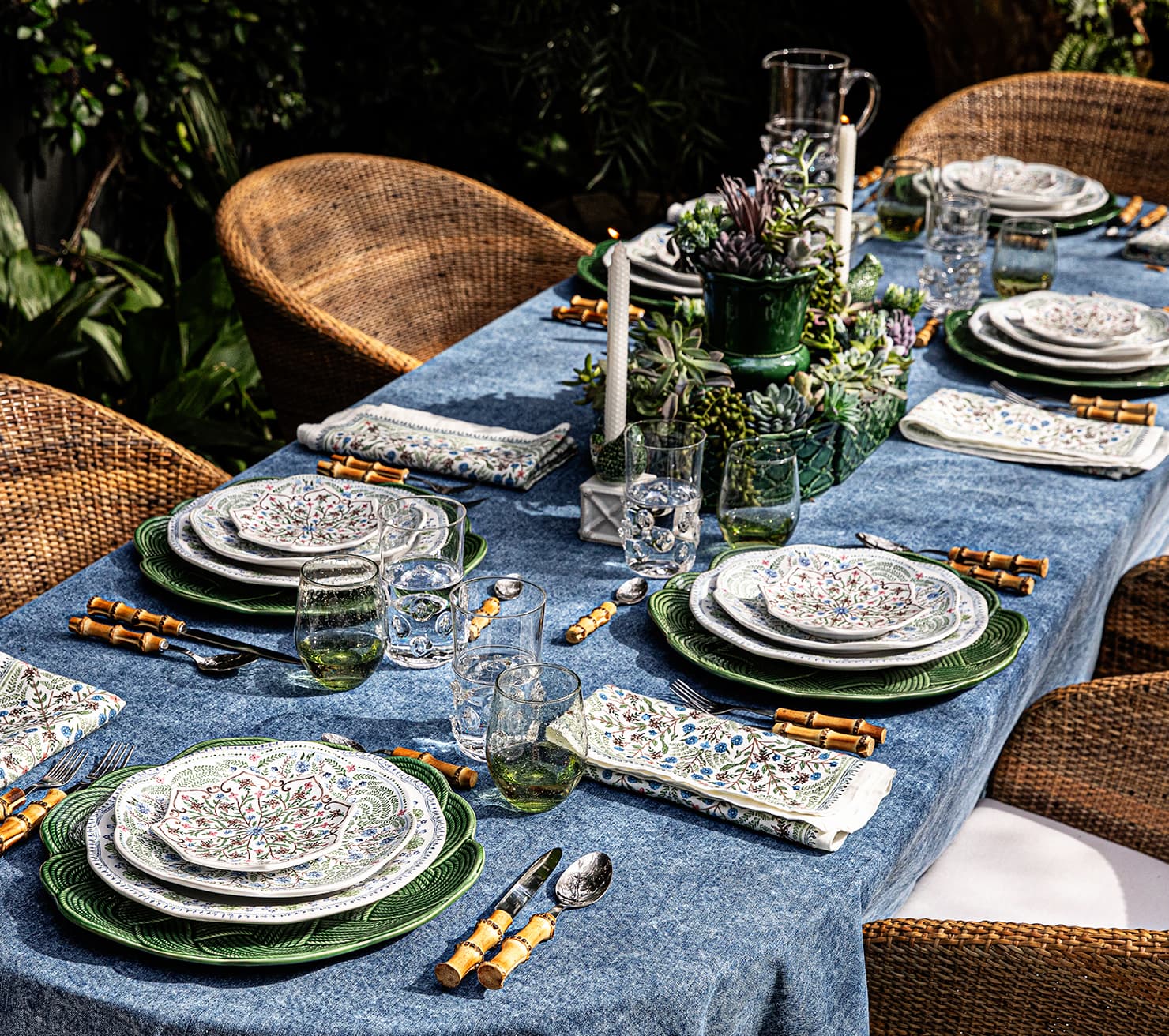 Elegant outdoor dining table setting with plates, glasses, and cutlery on a blue tablecloth.