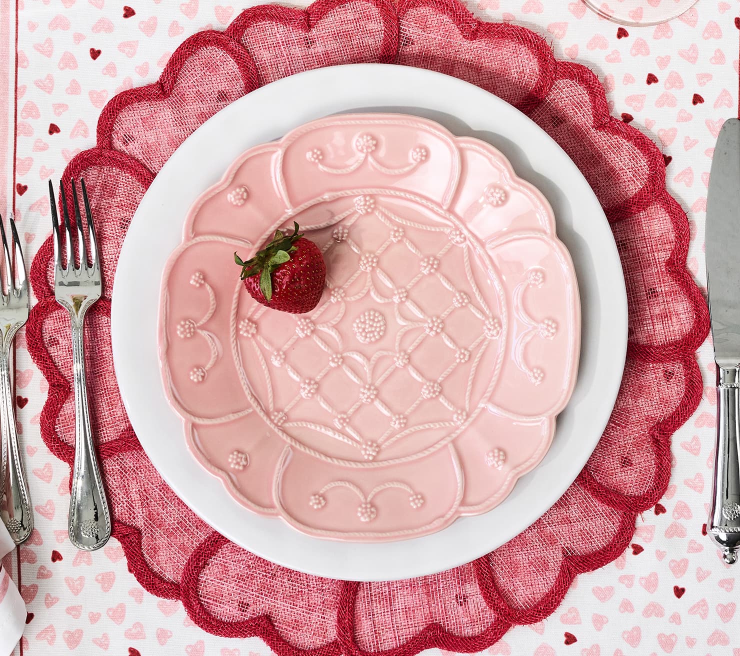 Pink decorative plate with a strawberry on a white plate, surrounded by red lace and heart-patterned tablecloth.