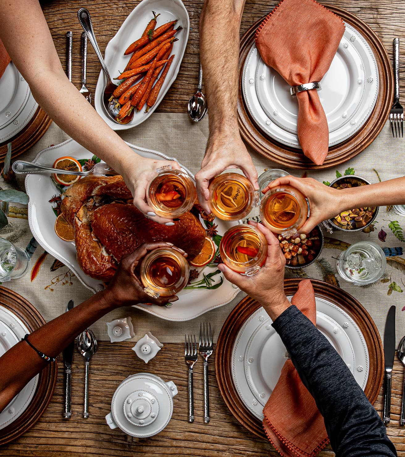 People toasting with glasses of wine at a festive dinner table with roasted turkey and carrots.