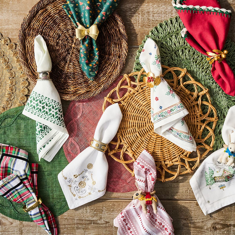 Decorative table setting with wicker placemats and embroidered napkins on a wooden surface.