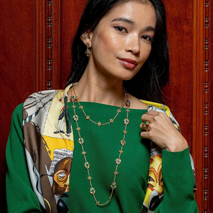 Woman wearing a green top with a colorful scarf and gold necklace against a red background