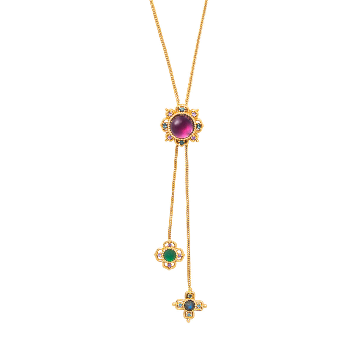 A gold lariat necklace featuring a large oval purple cabochon at the main pendant, with two dangling chains ending in floral and cross-shaped pendants set with green, blue, and small clear stones.