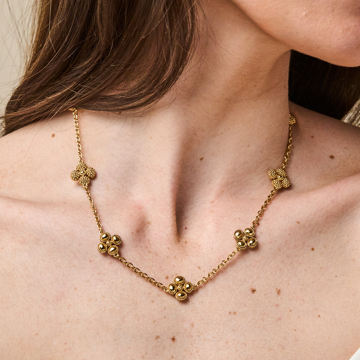 A gold necklace with five textured flower-like links and a central cluster, shown worn on a model's neck.