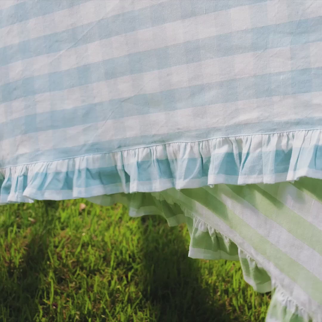 Load video: Video featuring woman setting the table in an outdoor garden. Blue plates, blue gingham tablecloth, and blue candlesticks are featured in the video.