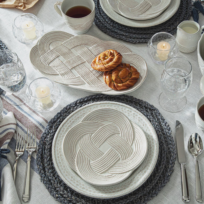 Video of elegant table setting with woven placemats, plates, and cutlery on a light surface.