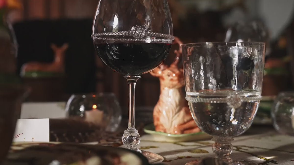 Load video: Video showcasing the Juliska Forest Walk Collection. A styled dining table setting with layered ceramic plates featuring a woodland deer and leaf pattern, wine glasses, a green duck-shaped centerpiece in a ceramic cup, and a deer figurine on a tablecloth with botanical print.