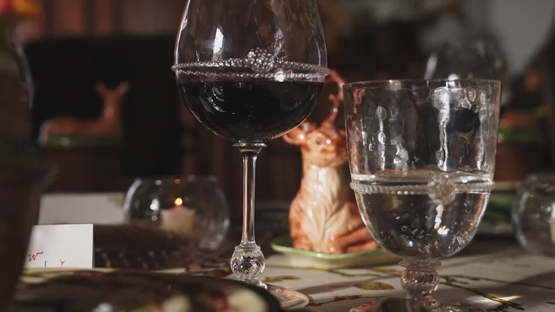 Load video: Video showcasing the Juliska Forest Walk Collection. A styled dining table setting with layered ceramic plates featuring a woodland deer and leaf pattern, wine glasses, a green duck-shaped centerpiece in a ceramic cup, and a deer figurine on a tablecloth with botanical print.