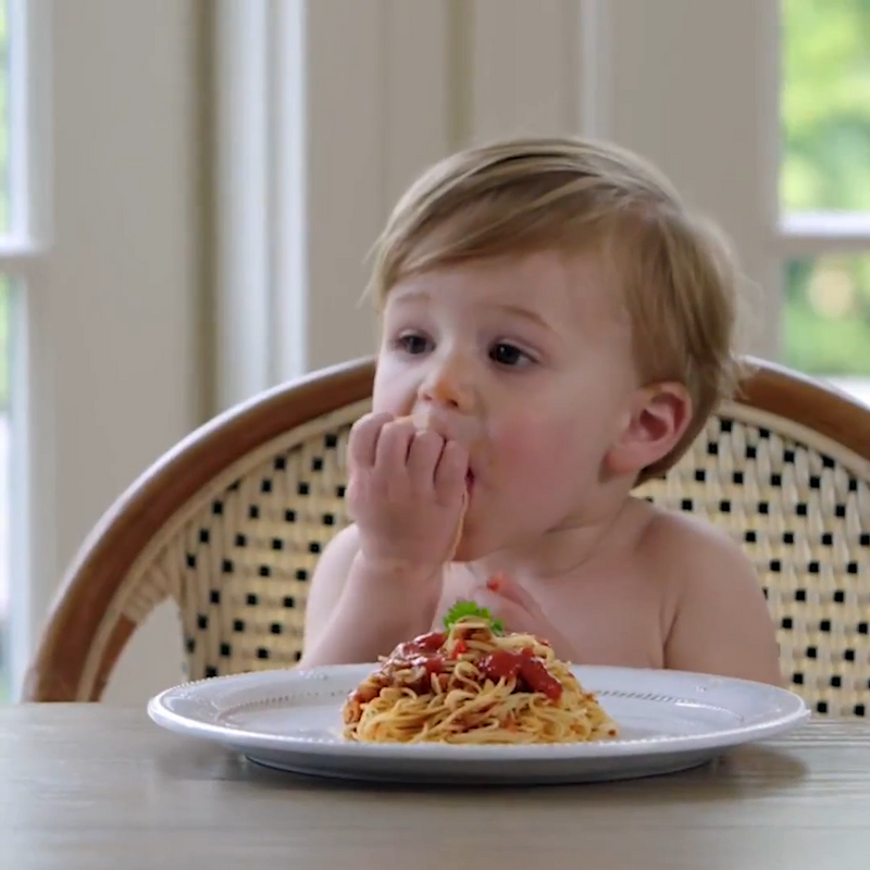 Toddler boy eats a plate full of spaghetti and red sauce on a melamine plate. 