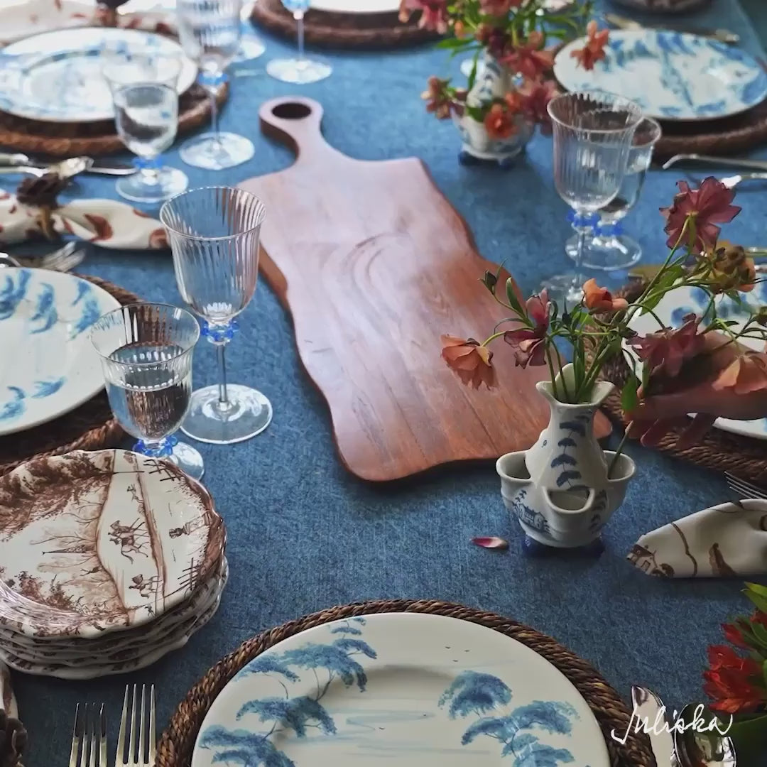 Load video: Moveable video featuring woman's hand setting and arranging the tablescape. The tablecloth is denim blue, the plates are brown and blue, and the glasses are clear with blue accents.