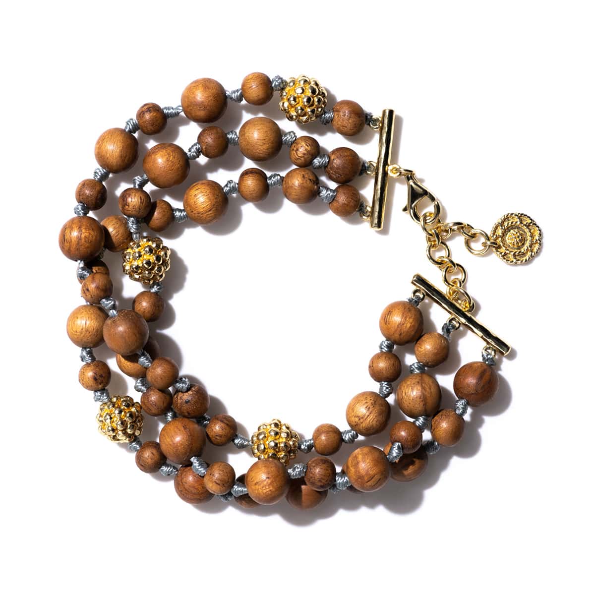 Hand-carved teak wood beads are strung and knotted like pearls and sprinkled with little golden berries for an effect that is simultaneously exotic and understated.